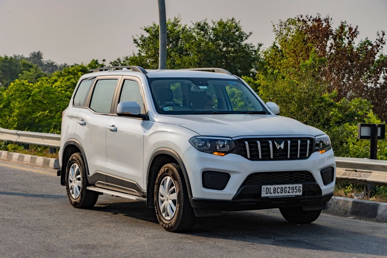 our-story White Mahindra SUV parked on a highway in Deeg, India, surrounded by lush greenery.